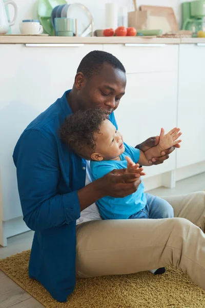 幸せなアフリカ系アメリカ人の父親の垂直肖像画とともに小さな男の子と一緒に家の床に座って スペースをコピー — ストック写真