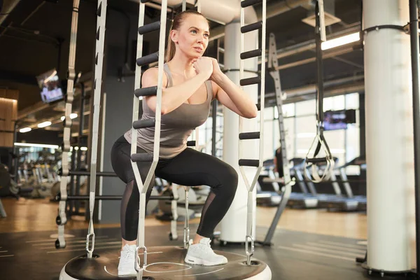 Full body strong sportswoman hanging on gymnastic rings and swinging while  exercising during intense training in dark gym stock photo