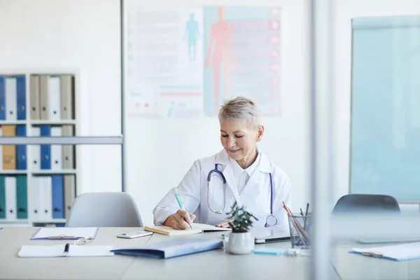 Porträtt Mogna Kvinnliga Läkare Skriva Anteckningar Och Ler När Sitter — Stockfoto