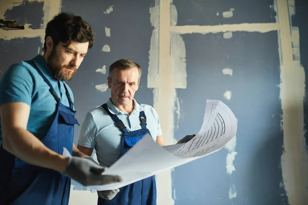 家を改装しながら計画を保持し 乾燥した壁に立っている2人の建設労働者の肖像 スペースをコピー — ストック写真
