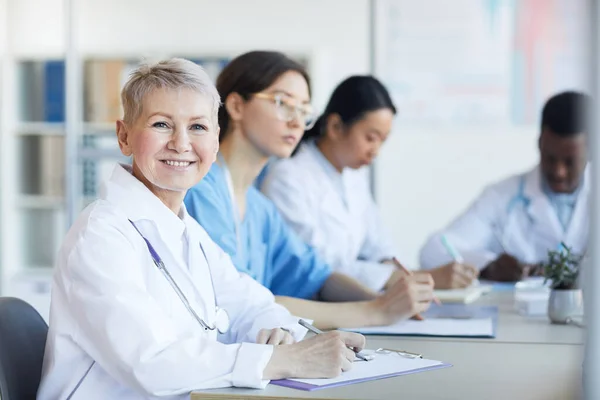 Retrato Doctora Madura Sonriendo Cámara Mientras Está Sentada Mesa Durante — Foto de Stock