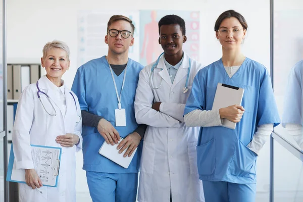 Multi-ethnic group of doctors looking at camera while posing together in clinic interior