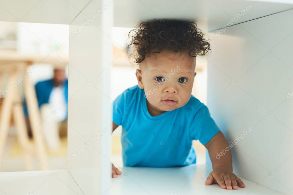 Portrait of cute African-American toddler peeking from box on childrens playground, copy space