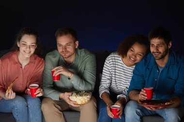 Evde film izleyen iki genç çiftin portresi aperatifler ve patlamış mısırlar yerken karanlık odadaki koltukta oturup, fotokopi çekerken.