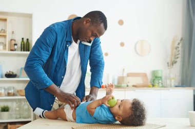 Orta yaşlı Afro-Amerikalı bir adamın bebek bezi değiştirirken karısını aramasının yan görüntüsü.