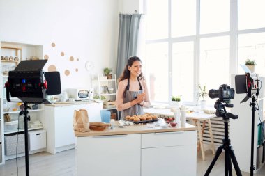 Profesyonel fırıncı mutfakta tek başına duruyor ve vlog kanalı için kek pişirme işlemini kameraya kaydediyor.