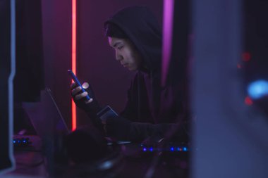 Siyahlı Asyalı bir adamın yan görünüm portresi ve kredi kartı, siber güvenlik konseptini hacklerken bilgisayar kullanması, boşluğu kopyalaması