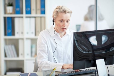 Ofisteki müşteri hizmetleri isteğini cevaplarken kulaklık takan ve bilgisayar kullanan kadın yöneticinin portresi, boşluğu kopyala