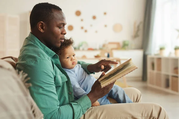 側ビューポートレートの思いやりのあるアフリカ系アメリカ人のお父さん読書本へかわいい赤ちゃん家 コピースペース — ストック写真