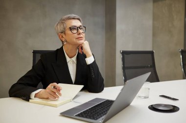 İş yerinde gri duvara yaslanırken dalgın dalgın bakan başarılı bir iş kadınının minimal portresi, boşluğu kopyala