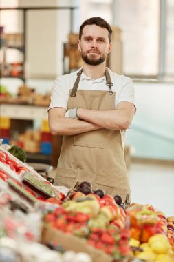 Çiftçilerin pazarında taze meyve ve sebze satarken kolları çapraz duran ve kameraya bakan sakallı adamın dikey beli.