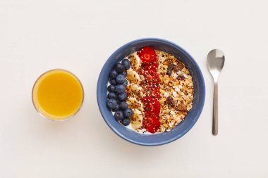 Beyaz arka planda portakal suyunun yanında meyve ve böğürtlenlerle süslenmiş lezzetli granola tatlısının minimal kompozisyonu, sağlıklı kahvaltı kavramı, kopyalama alanı