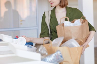Modern genç kadının orta bölüm portresi plastik eşyaları evde sıralıyor, geri dönüşüme hazır, boşluğu kopyalıyor