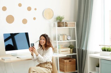 Kıvırcık saçlı neşeli bir kadının telefonda video uygulaması kullanarak konuşmasının yatay görüntüsü.