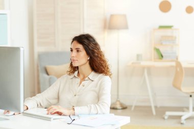 Evde bilgisayarla çalışan genç ve ciddi bir iş kadınının yatay görüntüsü.