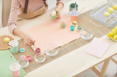 Paskalya için pastel renkte yumurta boyayan, mutfakta ya da resim stüdyosunda oturan, tanınmayan bir kadını yüksek açılı görmek.