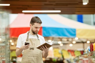 Süpermarkette envanter sayımı yaparken akıllı telefondan arayan sakallı adamın belden yukarı portresi.