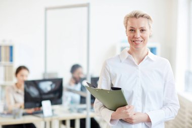 Arka planda bir grup ofis çalışanı ile kameraya gülümseyen başarılı kadın yöneticinin belden yukarı portresi, kopyalama alanı