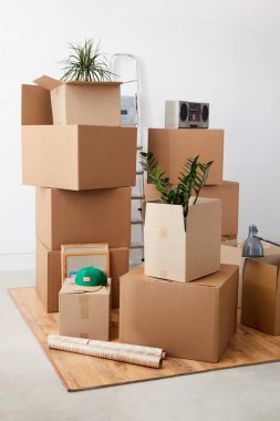 Vertical background image of cardboard boxes stacked in empty room with plants and personal belongings inside, moving or relocation concept, copy space clipart
