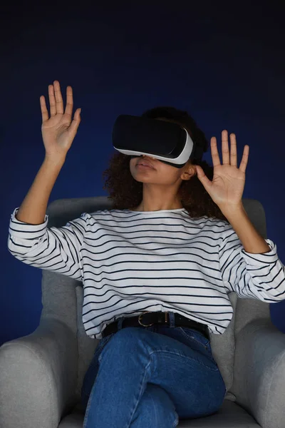Vertical portrait of mixed-race young woman wearing virtual reality gear while enjoying immersive videogame or movie in dark, copy space