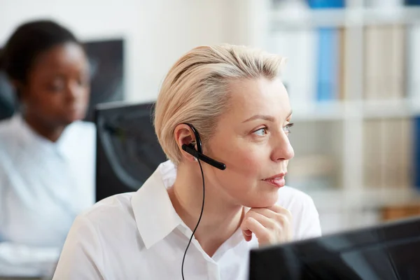 Close up portrait of blonde woman wearing headset and talking to customer while working in support service call center, copy space