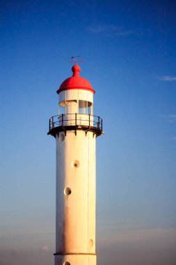 Kırmızı ve beyaz deniz feneri mavi gökyüzü günbatımı sırasında önünde