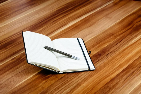 Apra il notebook e una penna su un tavolo di legno — Foto Stock