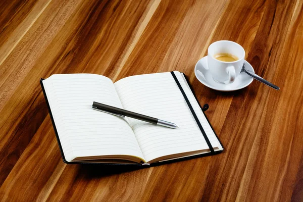 Black notebook, pen and a espresso on a wooden table
