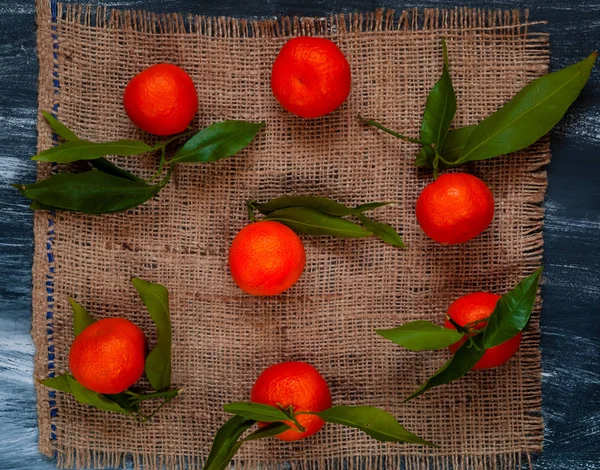 Mandariner med gröna blad på säckväv på en mörk trä bakgrund — Stockfoto