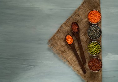 Tahta kaşık ve çuval bezi, sağlıklı beslenme kavramı üzerinde metal bardak içinde çeşitli tahıl. Üstten Görünüm. Serbest metin alanı olan rustik arka plan