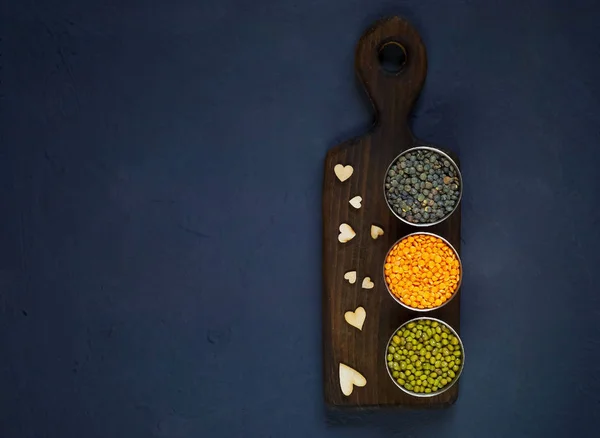 Concepto de comida vegetariana. Cereales y legumbres en copas de metal sobre una textura de madera con corazones sobre un fondo azul de hormigón. Vista superior, espacio vacío para texto — Foto de Stock