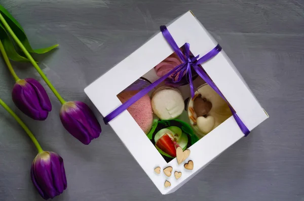 sweet dessert in a box and bouquet of ultraviolet tulips on a light background, space for text