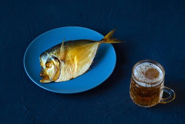 Mavi plaka ve bira cam kadehi mavi bir arka plan üzerinde füme balık