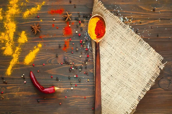 Wooden spoon on a texture of burlap and ingredients on a dark background. Background with spices, turmeric, star anise, pepper — Stock Photo, Image