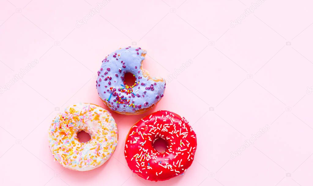 Bitten colored donuts with colorful sprinkles on pink background. Close-up