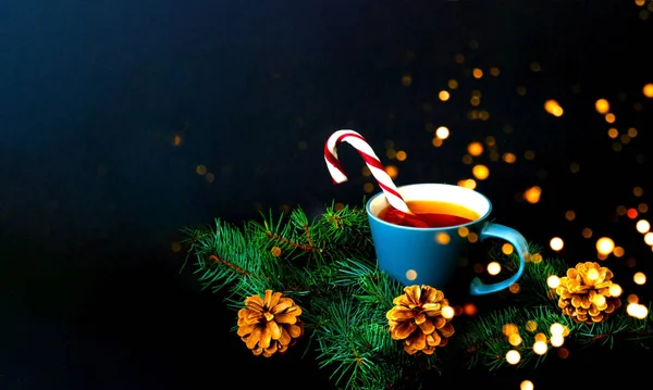 Bir fincan çay ve karamelli baston. Çam dallarından oluşan bir desen üzerine düşen karın arka planına karşı. Noel arkaplanı. Yakın plan.