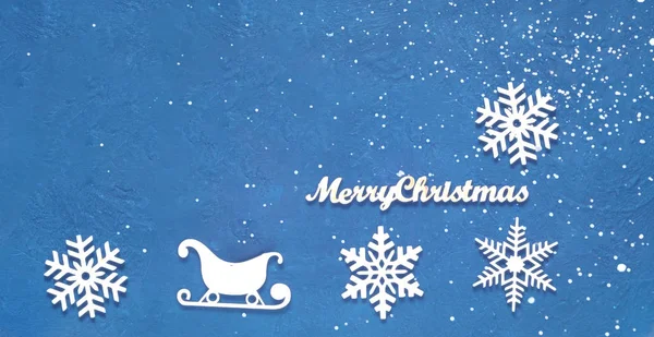 Des flocons de neige et des traîneaux de Noël décoratifs en bois sur fond bleu. Carte de Nouvel An festive en couleur tendance — Photo