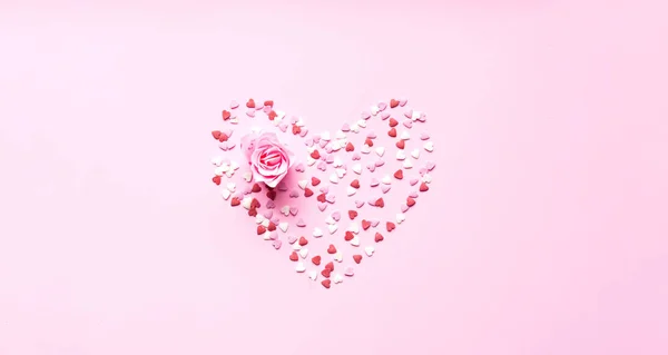 Валентинів день. Серцева форма сформована з солодкого конфетті на рожевому тлі з квіткою троянд. Шаблон: Приглушено вітальну картку або текстовий дизайн. Копіювальний простір — стокове фото