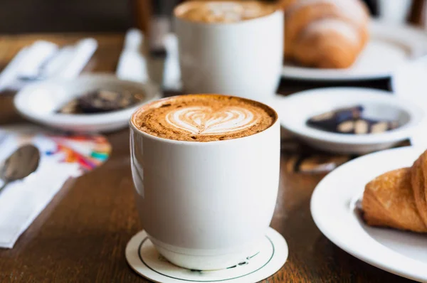 Vit kopp kaffe med crema och croissant. suddig bakgrund av caféet.Närbild — Stockfoto