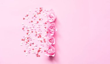Sevgililer Günü. Pembe arka planda gül çiçeğiyle tatlı konfetiden oluşan kalp şekli. Tebrik kartı ya da metin tasarımının şablonu