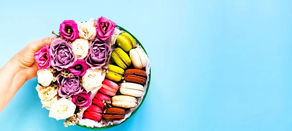 Festive composition. Female hand holds gift box with roses and macaroons. Valentines day concept. Close-up