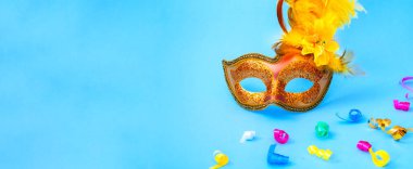 Golden Carnival mask on blue background with with colored confetti. Mardi gras festive concept. Copy space