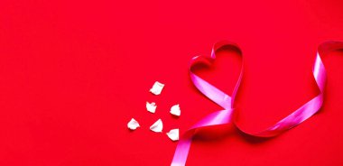 Kırmızı arka planda beyaz gül yapraklarıyla kalp şeklinde şenlikli pembe kurdele. Anneler Günü konsepti. Tebrik kartı ya da metin tasarımının şablonu. Yakın plan, kopyalama alanı