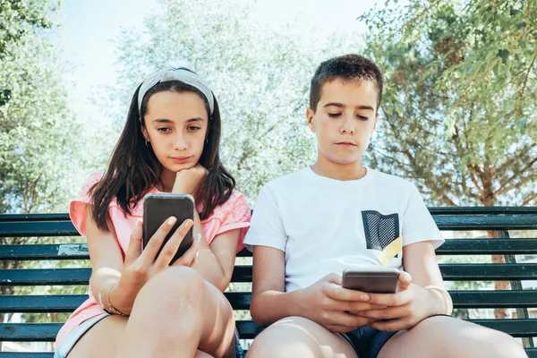 Niños mirando un celular sentado en un banco en el parque — Foto de Stock