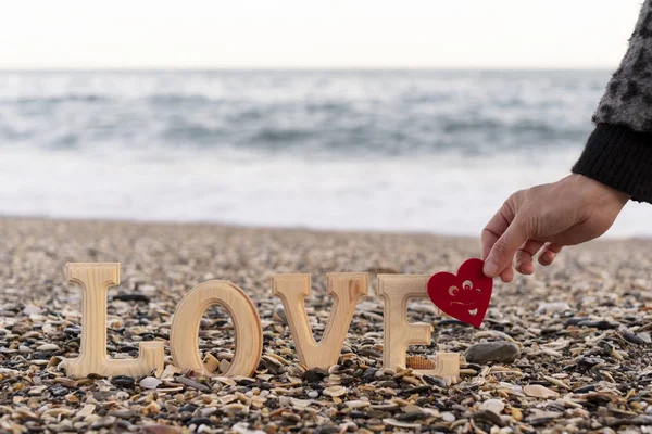 Wooden letters forming the word love and a hand holding a red heart on the seashore. concept of st. valentine's day — Stock Photo, Image