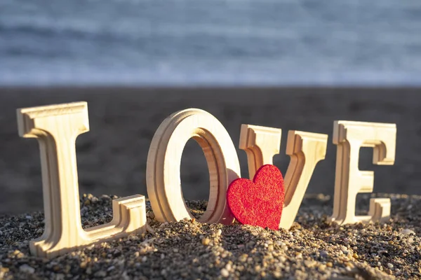 Wooden letters forming the word love with a red heart on the seashore. concept of lovers — Stock Photo, Image