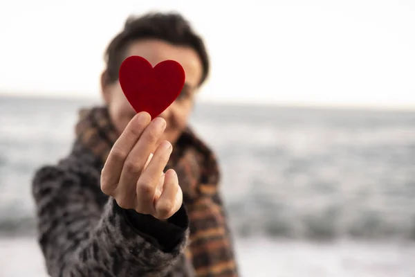 Woman's hand holding a red heart on the seashore. concept of valentine's day — Stock Photo, Image