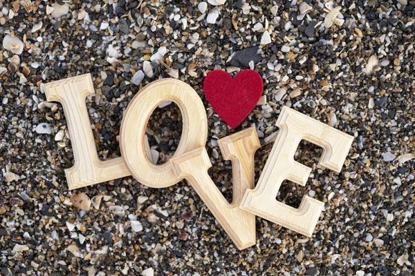 Wooden letters forming the word love with a red heart on a background of beach sand. concept of san valentine — Stock Photo, Image