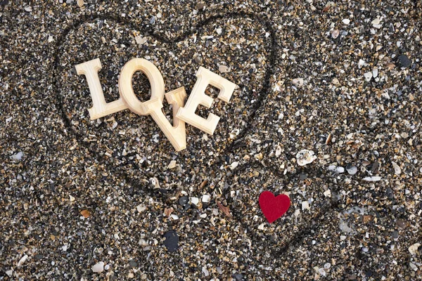 Wooden letters forming the word love with a red heart on a background of beach sand, inside a heart made with the fingers. concept of san valentine — Stock Photo, Image