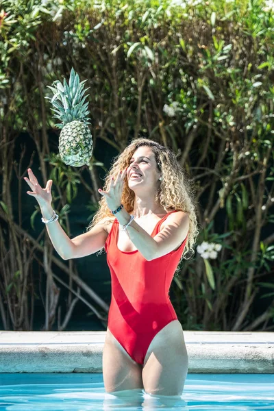 Frau in rotem Badeanzug wirft Ananas in die Luft in einen Pool — Stockfoto